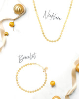 Simone necklace and bracelet in 14k gold finish with ribbons and ornaments on a white background