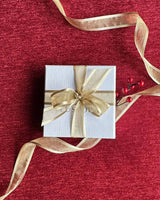 White Lustora jewelry box with gold ribbon on a festive, red background